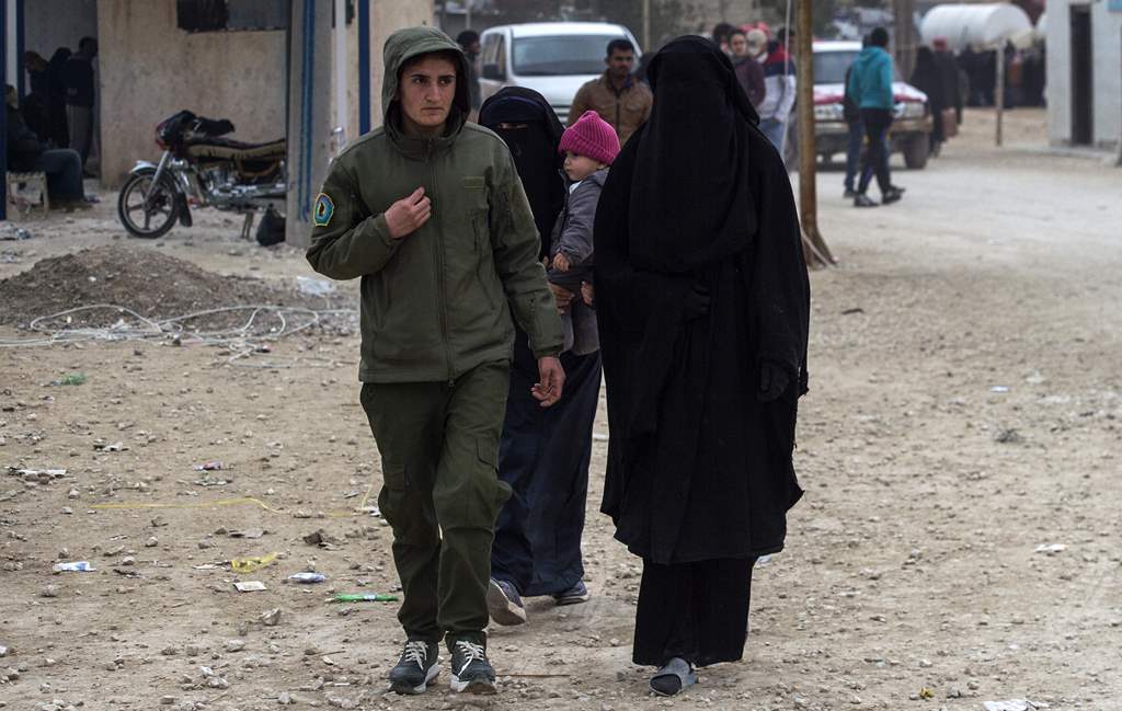 مقاتلة من القوات الكردية ترافق زوجات أحد قيادات داعش في مخيم للاجئين في الحسكة بسوريا. (أ.ف.ب)