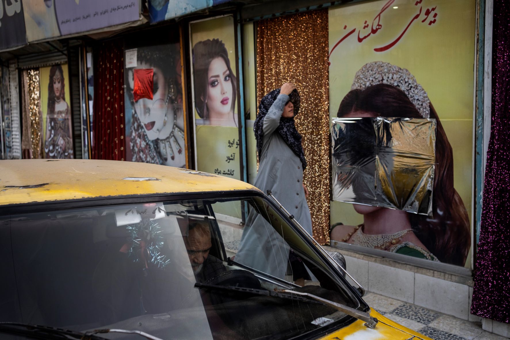 أفغانية تعدل حجابها أمام صالون تجميل في كابول. وقد عمدت "طالبان" إلى تشويه صور النساء على الجدران أو تغطيتها.