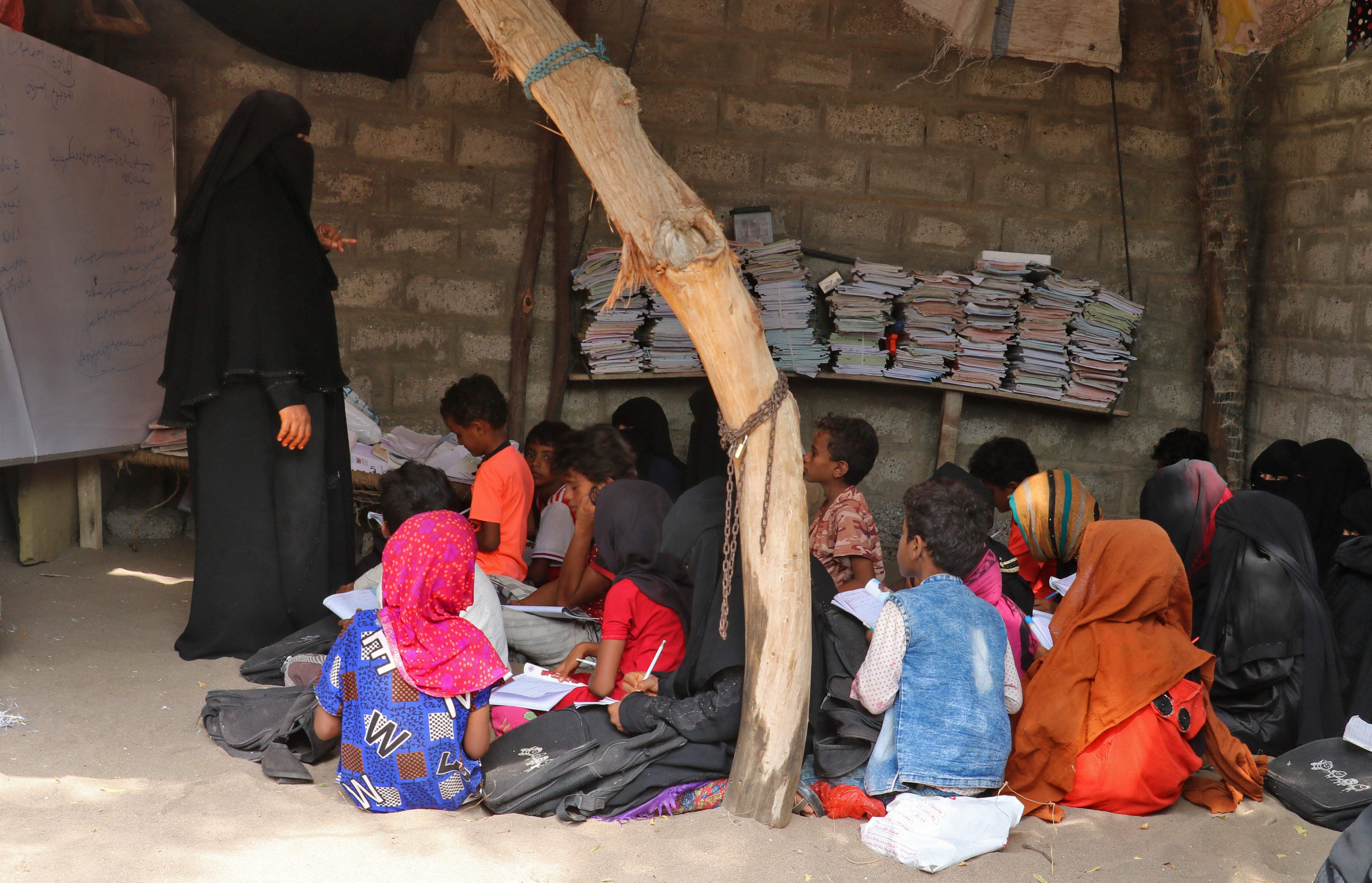 عدد من الطلاب يجتمعون في أحد الظلال بفناء منزل آمنة (أ ف ب)