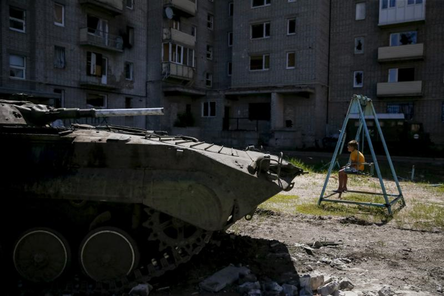 صبي يجلس على أرجوحة بالقرب من مبنى سكنه الذي تضرر أثناء القتال بين الجيش الأوكراني والانفصاليين الموالين لروسيا، ويلهو بجانب ناقلة جند مدرعة أوكرانية، بالقرب من "دونيتسك"، شرق أوكرانيا، يونيو (حزيران) 2015. 
