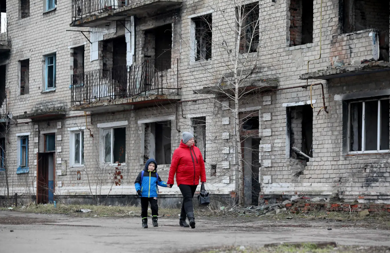 امرأة وصبي يمران قرب مبنى قديم مدمر في بلدة "كراسنوغوريفكا" الصغيرة في دونيتسك