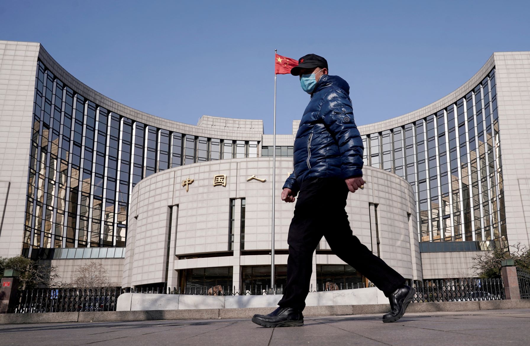 رجل مرتدٍ كمامة يسير أمام مبنى "بنك الشعب الصيني"، وهو المصرف المركزي للبلاد، في بكين أثناء إغلاق كورونا الجديد في 03 فبراير 2022 