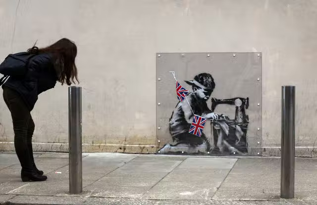 The former piece - Slave Labour (Bunting Boy) - which was attributed to Banksy - appeared on the same wall 10 years ago.png