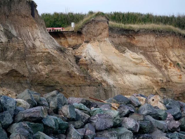 The end of a tarmac road shows the devastation caused by coastal erosion of the cliff face in the village of Happisburgh in 2019.png
