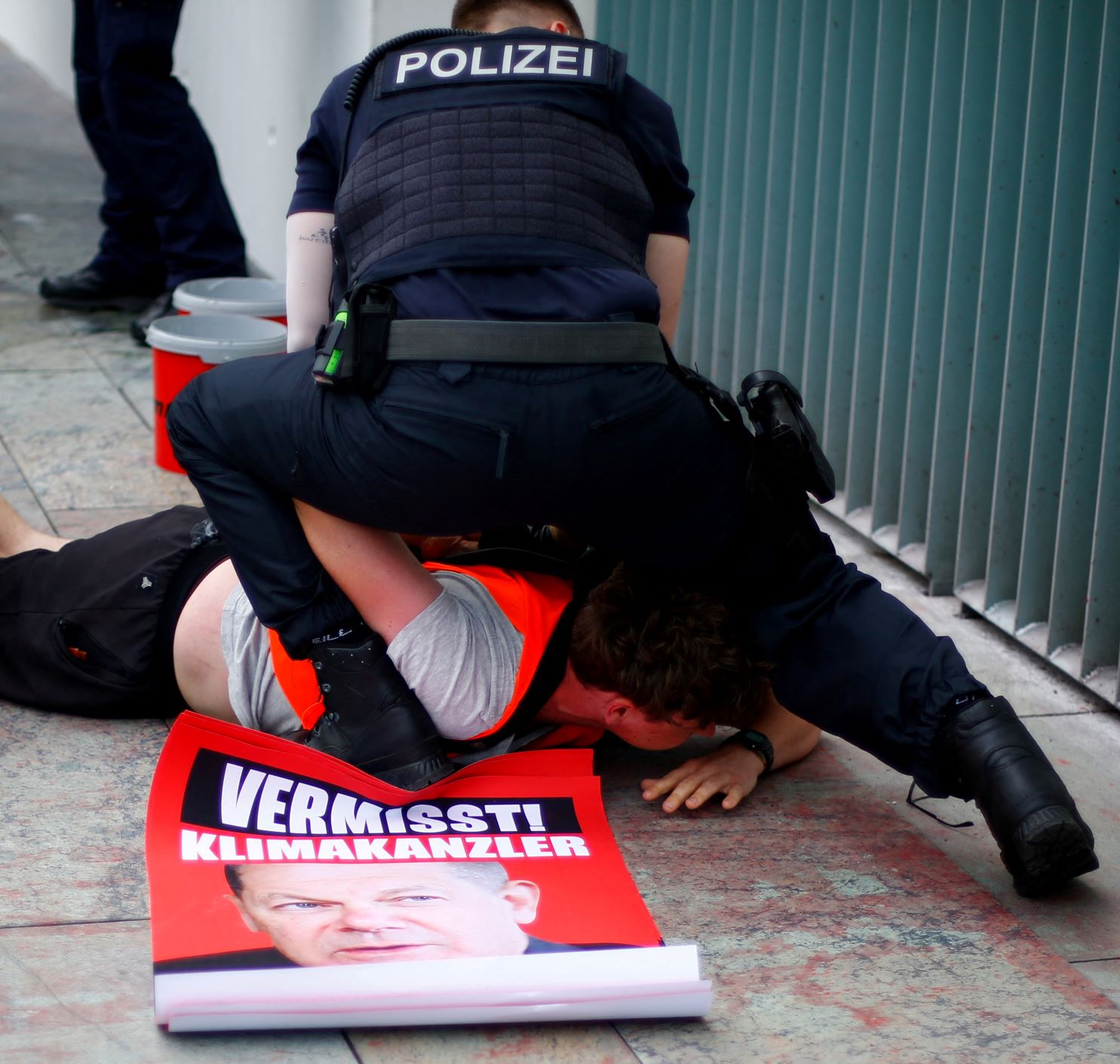 ضابط شرطة يحتجز أحد نشطاء حركة الجيل الأخير الذي رفع يافطة عليها شعار "أوقفوا جنون الوقود الأحفوري" أمام مقر المستشارية الألمانية في برلين بتاريخ 25 يونيو 2022 