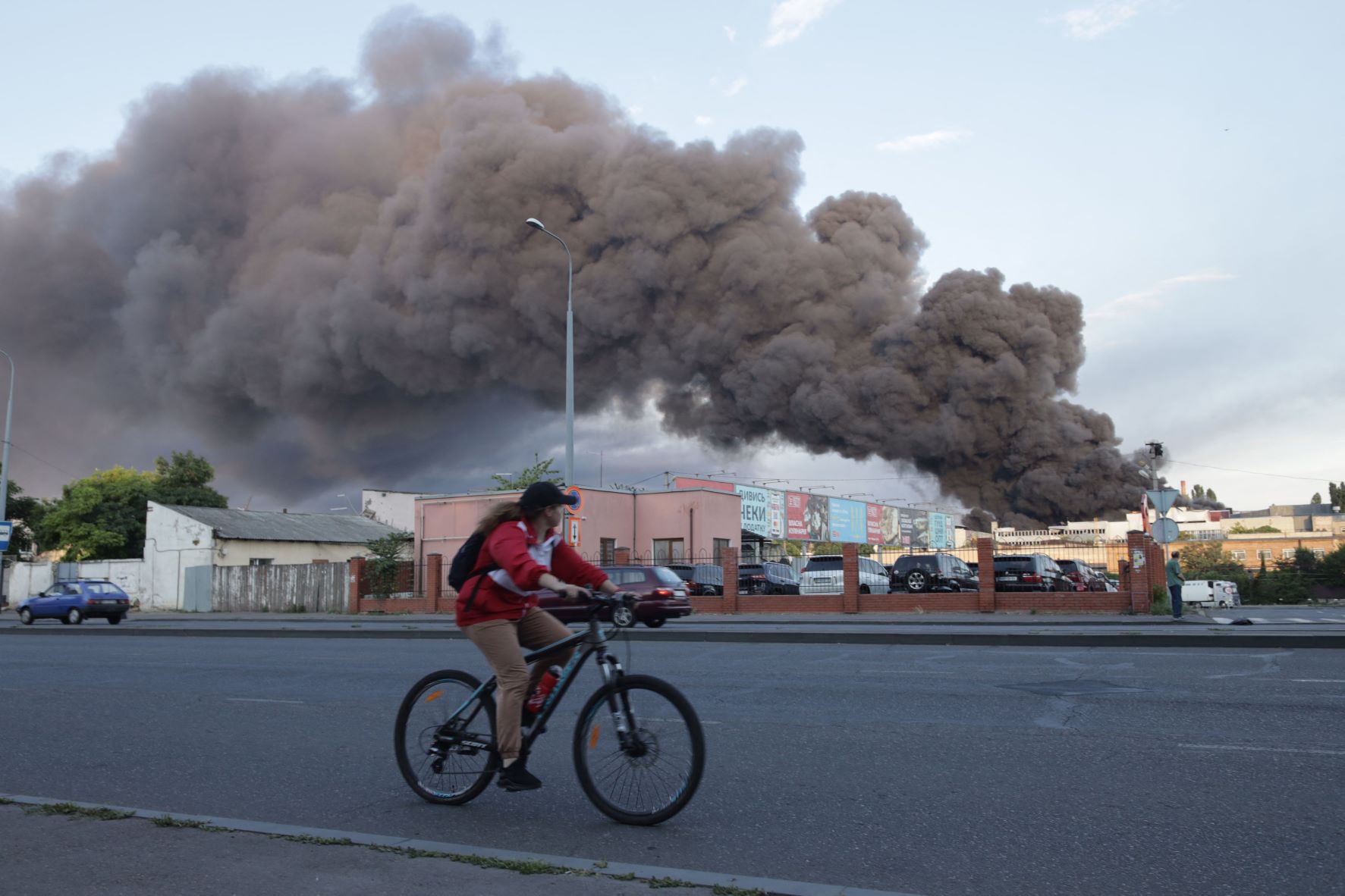 امرأة تقود دراجة هوائية قرب مكان يتصاعد منه دخان حريق نجم عن صاروخ روسي قصف شركة للتجارة والصناعة في أوديسا خلال الغزو الروسي لأوكرانيا بتاريخ 16 يوليو 2022 
