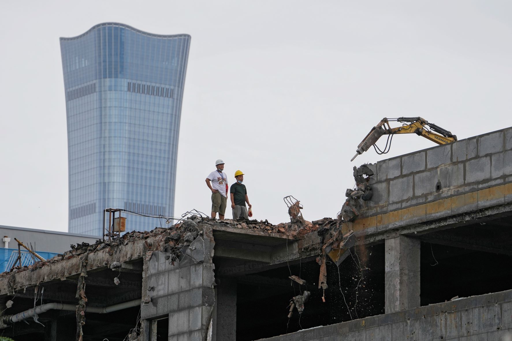 عمال بناء يراقبون حفارة تهدم مبنى وبدت خلفهم ناطحة السحاب شاينا زون تاور التي تعتبر الأطول في الصين بتاريخ 28 يوليو 2022 