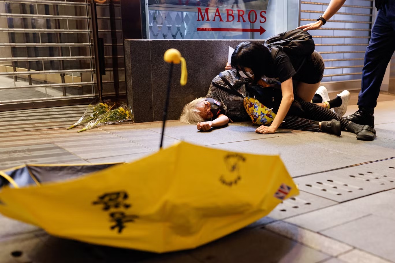 أحد المحتجين يرقد على الأرض في هونغ كونغ بعد دفعه خلال تظاهرات ضد "كوفيد" في البر الرئيس للصين (رويترز)