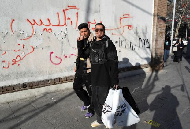 أناس يمرون أمام غرافيتي معادية لبريطانيا كتبت على جدار سفارتها في طهران من قبل موالين متشددين للنظام الإيراني بتاريخ 23 فبراير 2023 