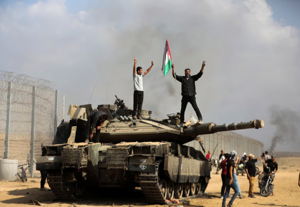 فلسطينيون يلوحون بعلمهم الوطني ويحتفلون بجوار دبابة إسرائيلية مدمرة عند السياج الجنوبي لقطاع غزة 