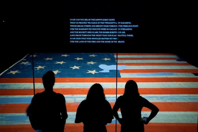 زوار يقفون أمام العلم الأميركي في واشنطن العاصمة، يونيو 2023 (رويترز)