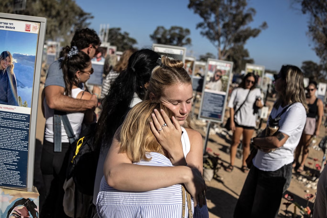 أفراد يتعانقون بجوار نصب تذكارية أقيمت لضحايا هجمات السابع من أكتوبر 2023 في موقع "مهرجان نوفا" في رعيم جنوب إسرائيل، في الذكرى الثانية لتلك الهجمات عام 2025 (أ ف ب/ غيتي)